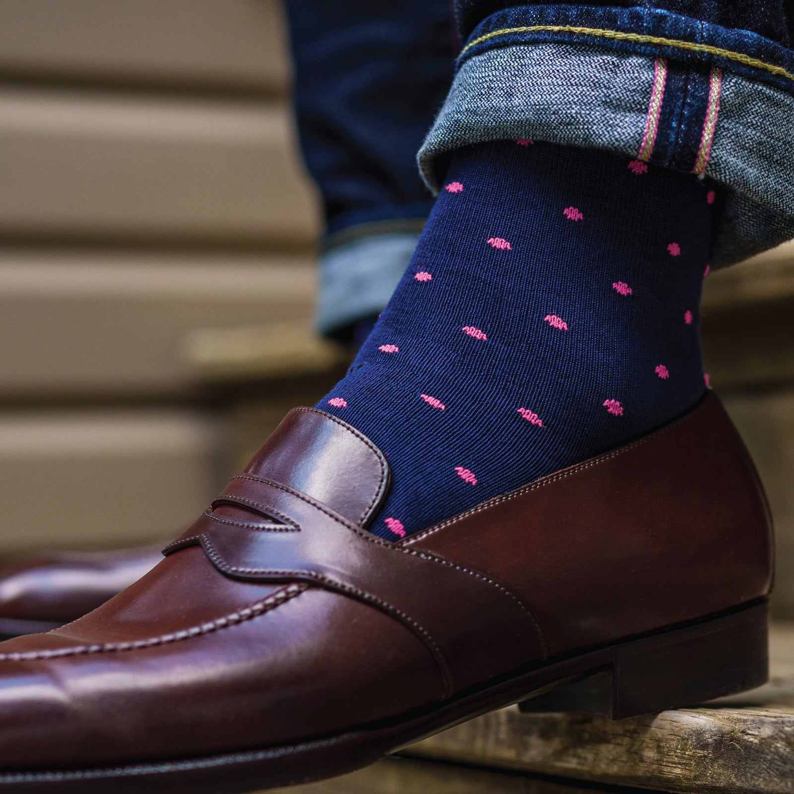 close up of a person wearing jeans and navy mid-calf dress socks with bright pink dots