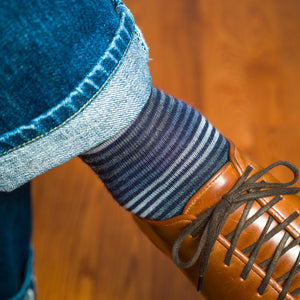 close-up of man wearing blue and grey horizontal striped dress socks with jeans and brown leather sneakers