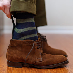 man wearing navy and olive horizontal striped dress socks using shoe horn to slide on brown suede chukka boots