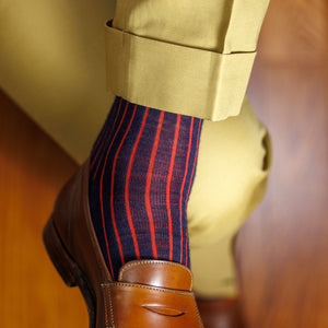 man crossing legs wearing navy and red shadow stripe dress socks with tan slacks and brown penny loafers