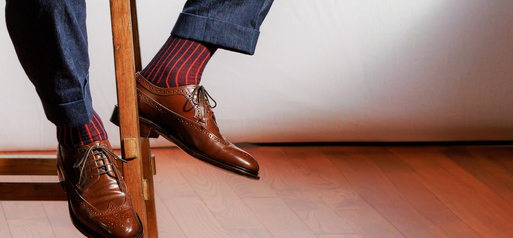 man seated on stool showing navy and red shadow stripe men's dress socks with slacks and brown wingtips