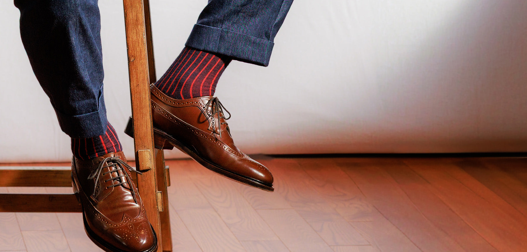 man wearing navy and red shadow stripe dress socks sitting on stool showing socks and dress shoes