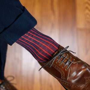 man crossing legs wearing navy and red shadow stripe dress socks with brown wingtips and navy slacks