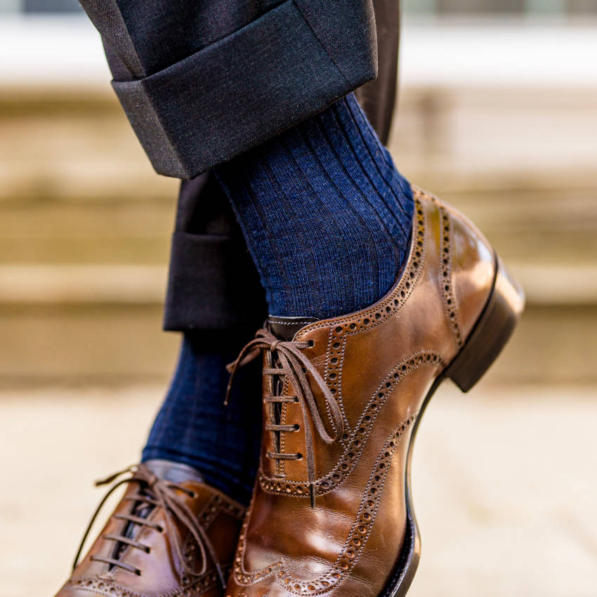 man crossing ankles wearing ribbed navy dress socks and light brown wingtips
