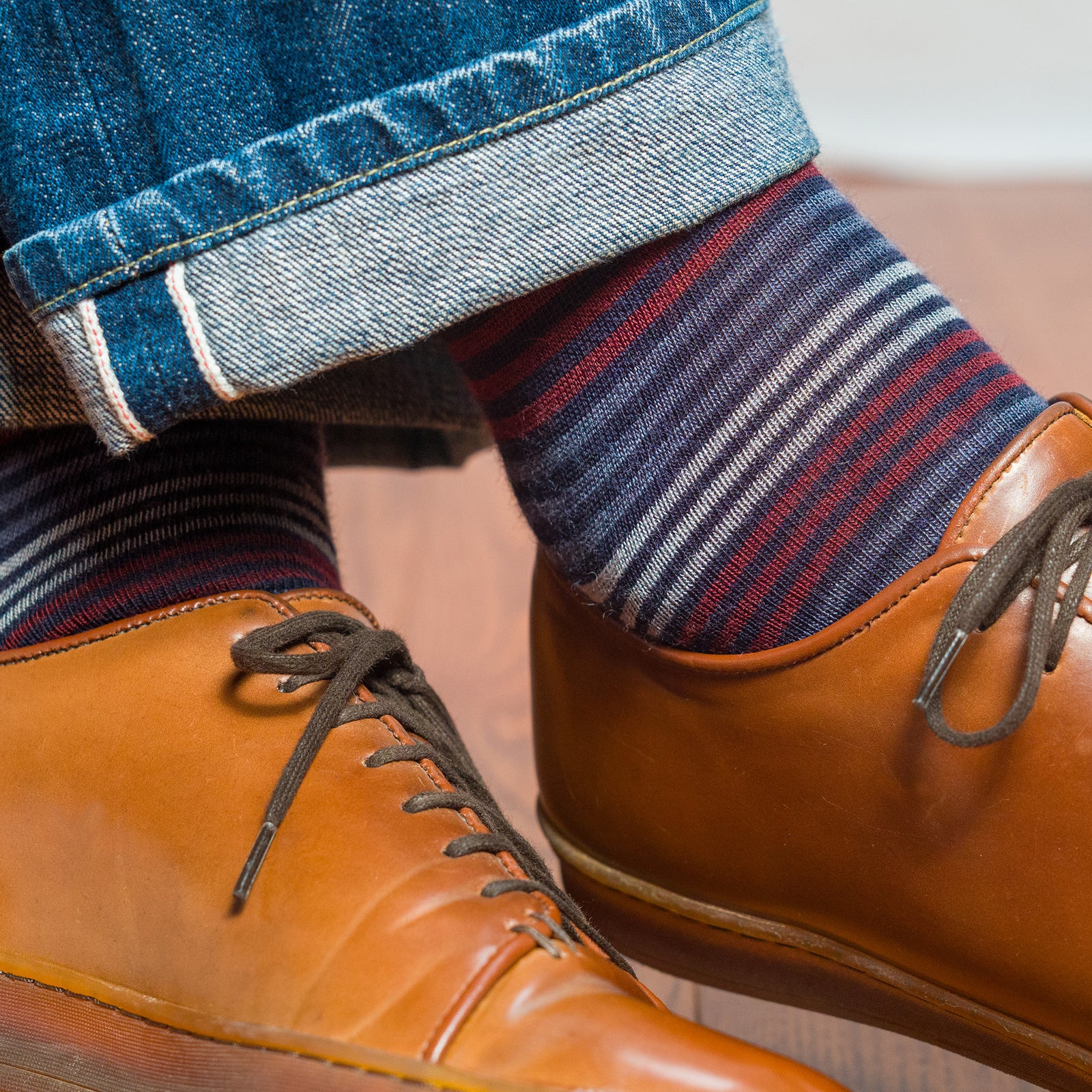 close-up of colorful striped dress socks worn with brown leather sneakers and rolled-up jeans