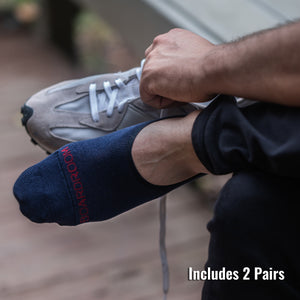 man putting on grey sneakers while wearing navy merino wool no-show dress socks