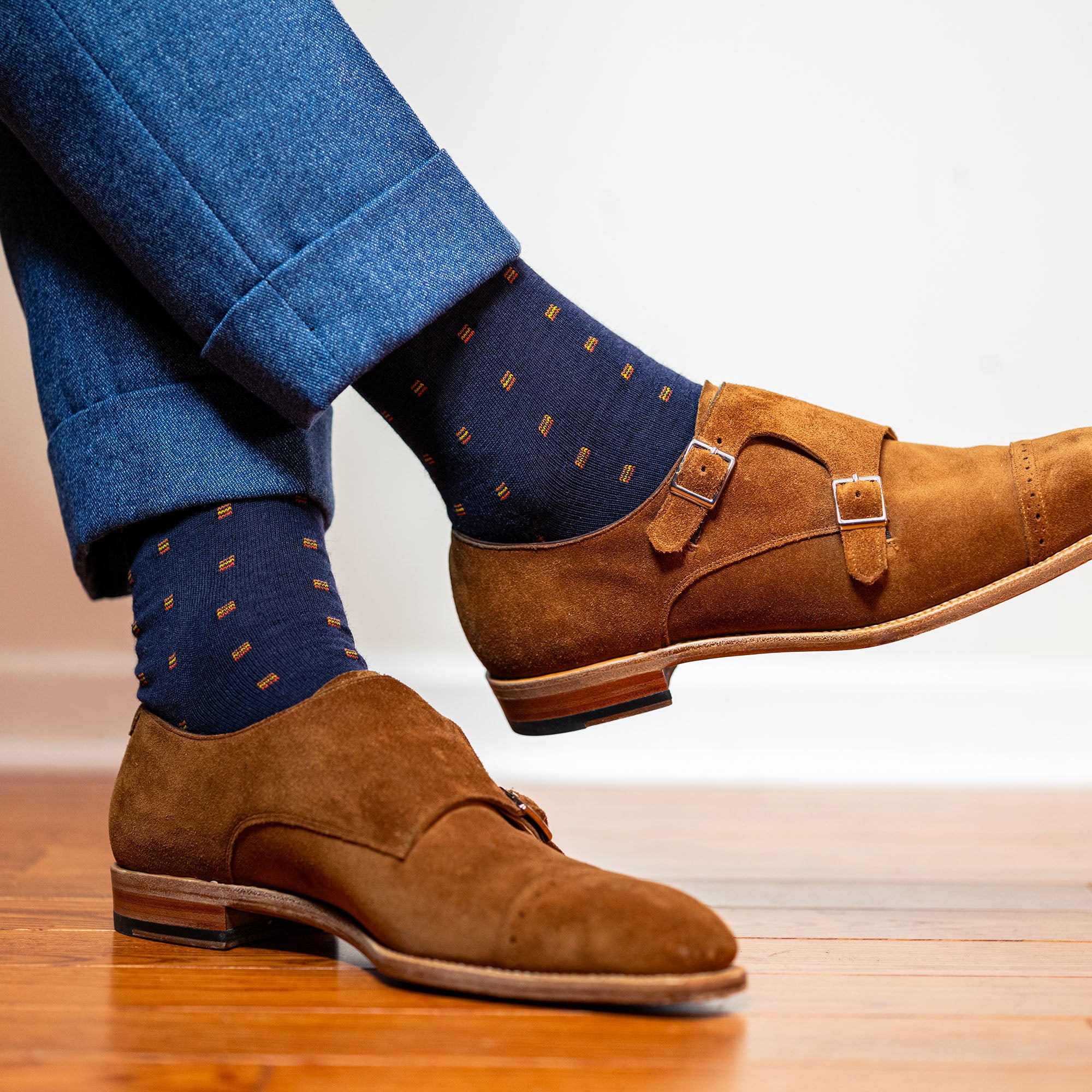 man crossing legs wearing navy and orange dress socks with light brown suede shoes