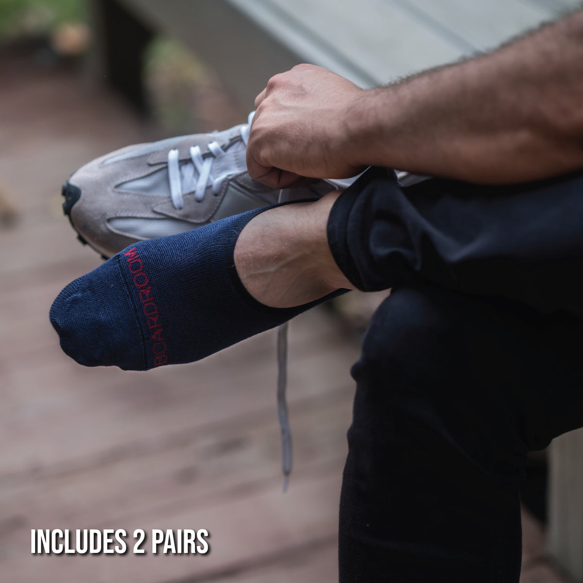 man sitting own putting on tennis shies wearing premium merino wool no-show socks in navy