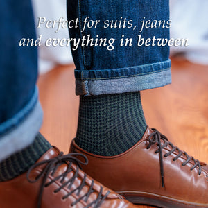 man standing on hardwood floor wearing olive and navy houndstooth dress socks with jeans and brown leather sneakers