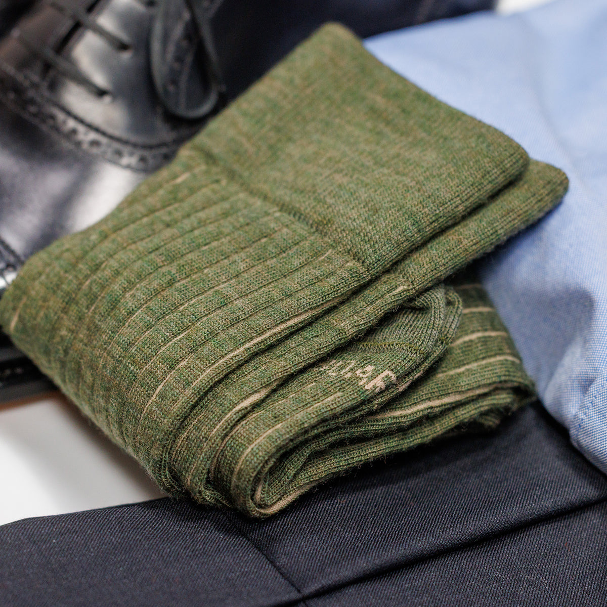 folded pair of olive and tan shadow stripe dress socks atop business casual outfit
