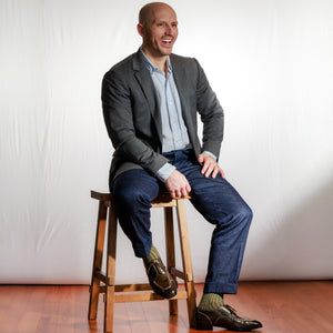 man wearing olive and tan shadow stripe dress socks with business casual outfit sitting on stool