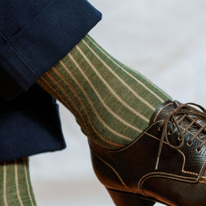 man crossing legs wearing olive and tan shadow stripe dress socks with navy suit and brown derbies