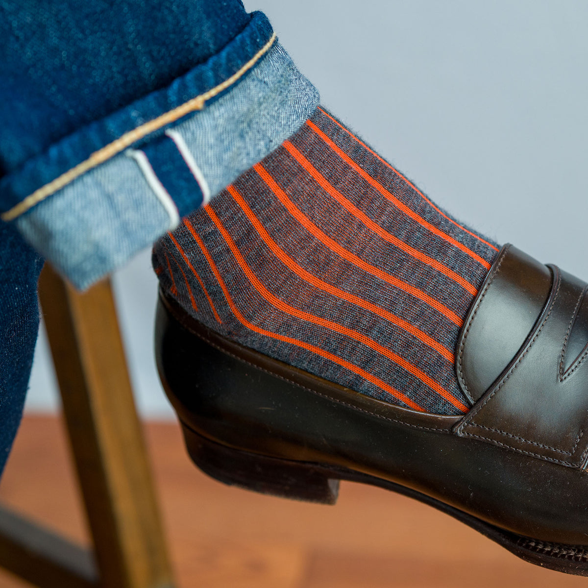 close up of grey and orange shadow stripe dress socks worn with jeans and brown penny loafers