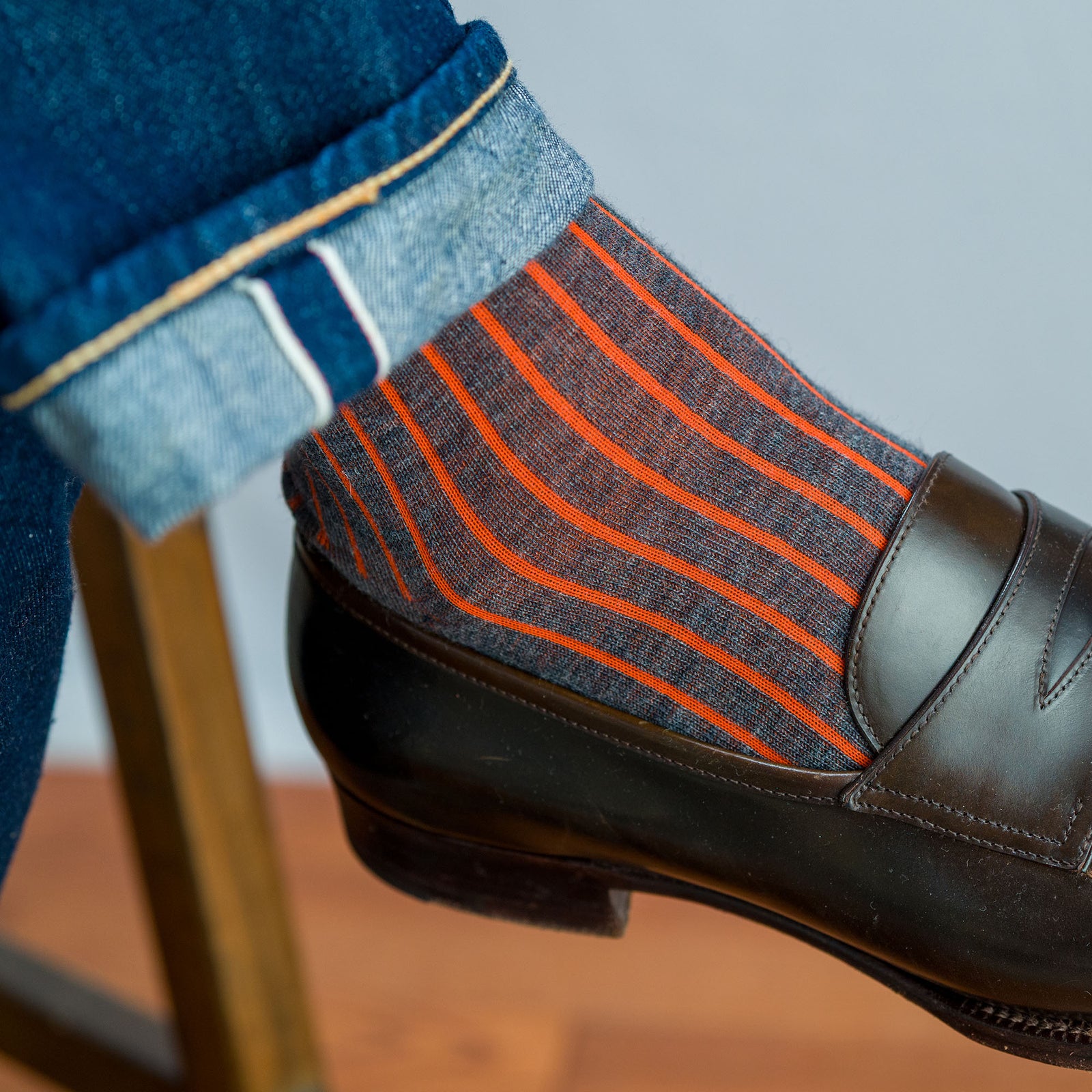 close up of grey and orange shadow stripe dress socks worn with jeans and brown penny loafers