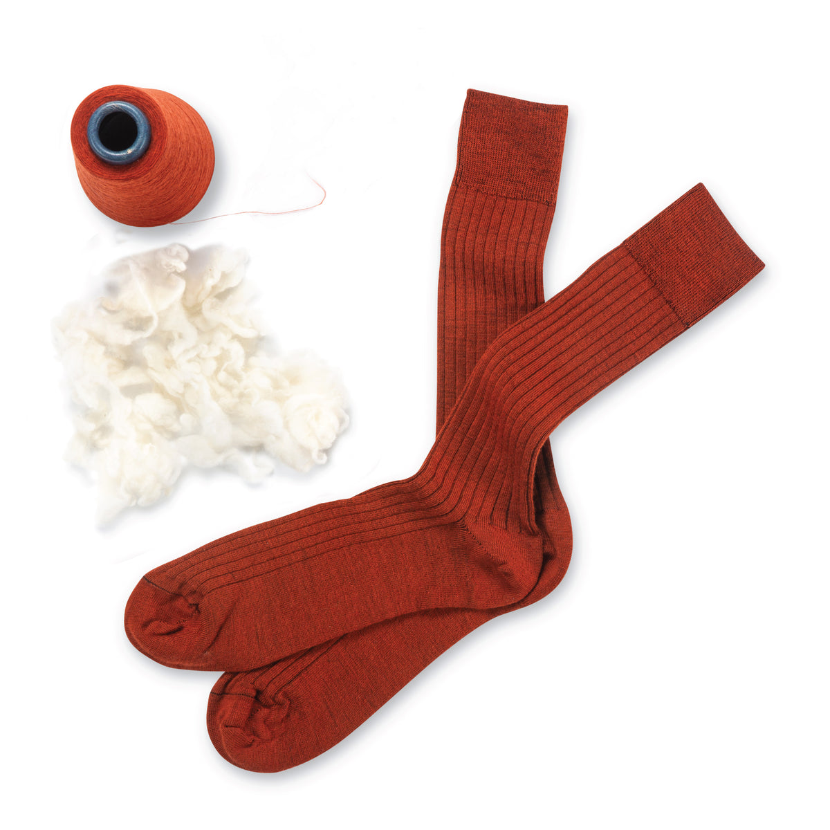 a pair of orange merino wool mens dress socks laying on a white background with wool and yarn next to it