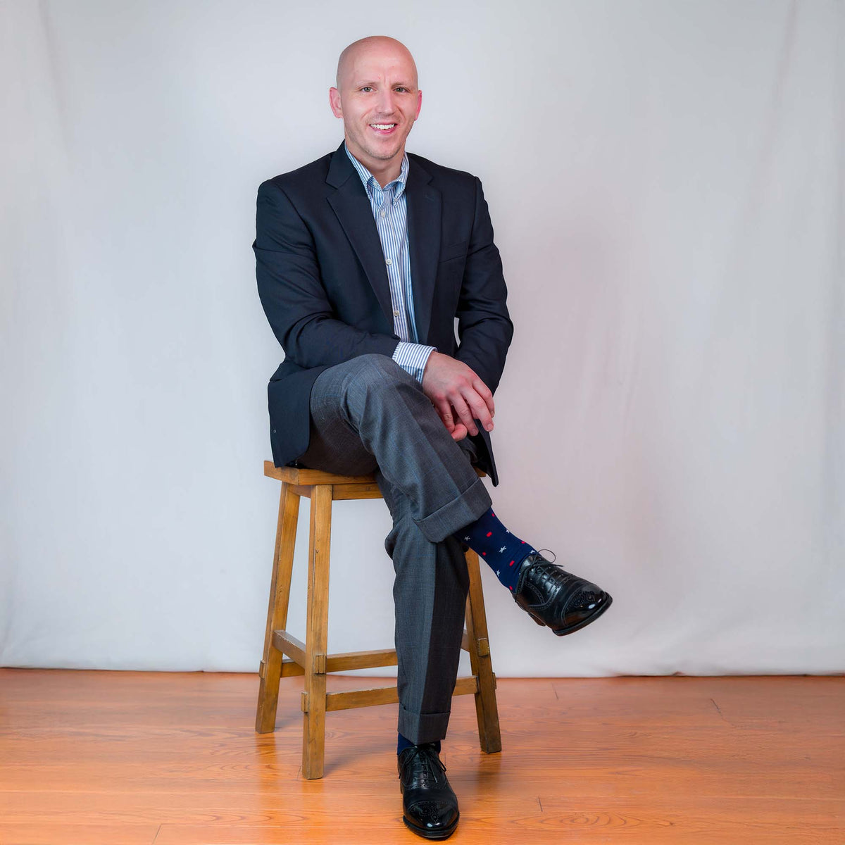man sitting on a stool in nice dress clothes wearing navy cotton star and dot patterned dress socks 