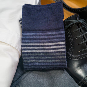 pair of blue and grey striped dress socks atop black dress shoes and business attire