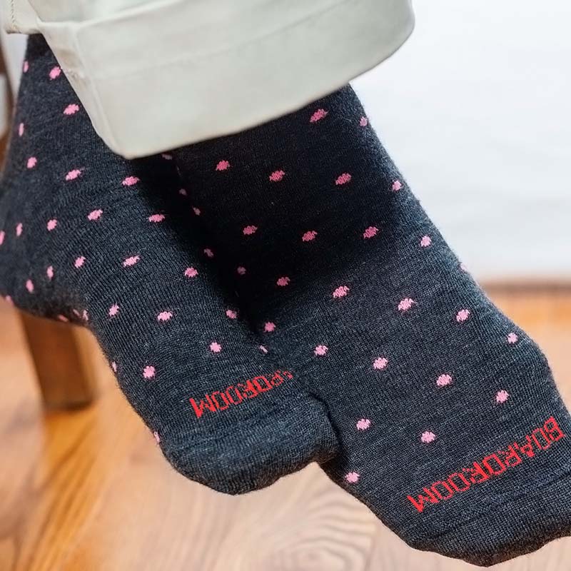 man wearing charcoal grey dress socks decorated with pink dots, crossing his legs while seated on a stool