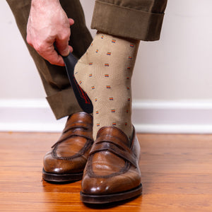 man wearing khaki patterned dress socks using shoe horn to put on brown penny loafers