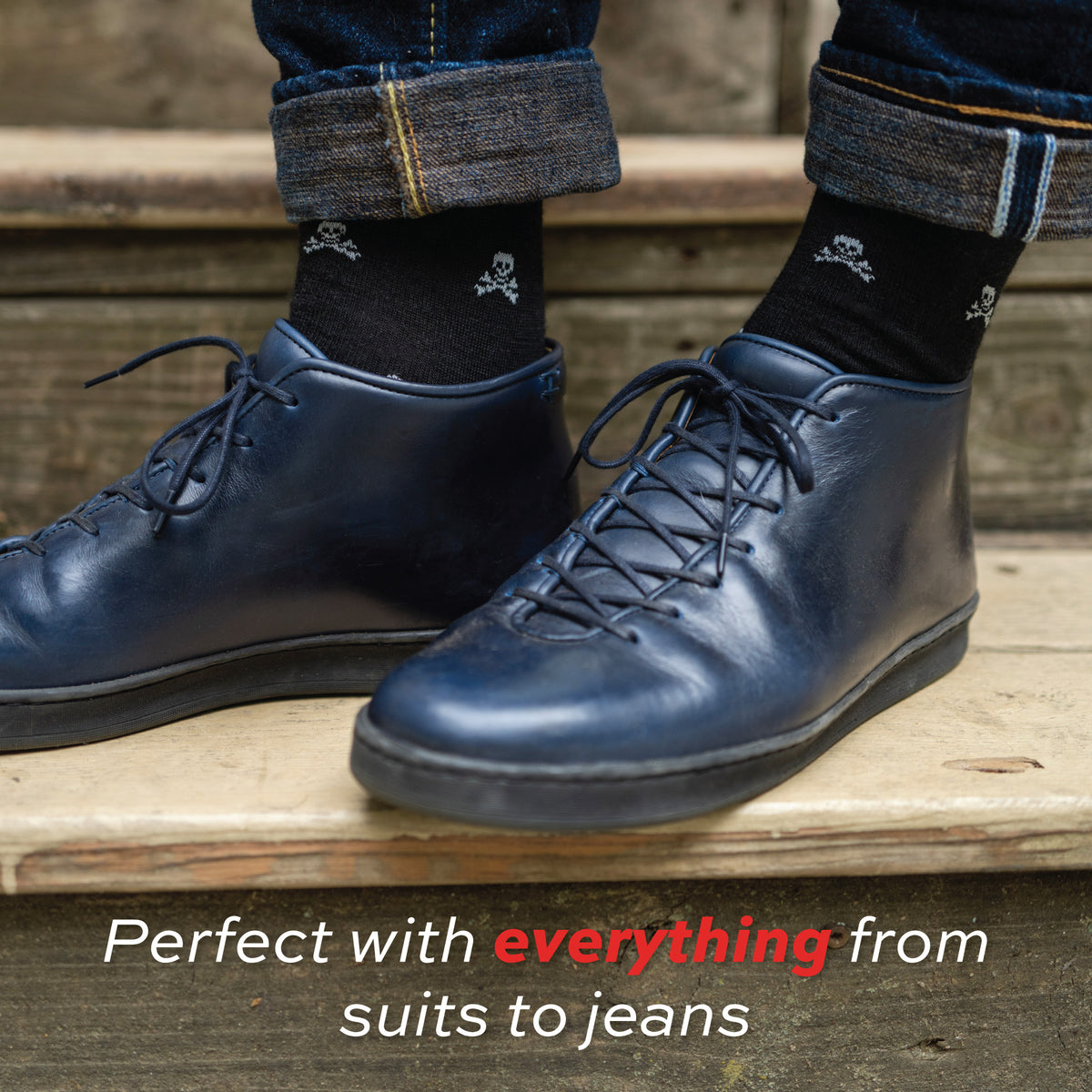 man standing on stairs wearing jeans and black over the calf merino wool dress socks with skull and bones pattern with "perfect with everything" text overlay