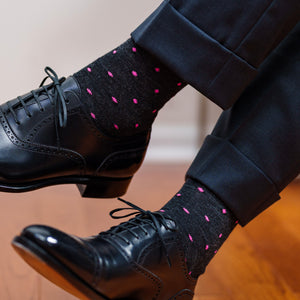 man crossing legs wearing dark grey merino wool dress socks decorated with bright pink dots