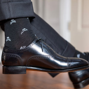 professional man crossing legs wearing skull dress socks with black oxfords and charcoal grey slacks