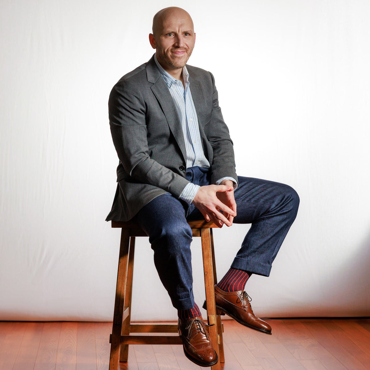 professional man wearing navy and red shadow stripe dress socks with business casual attire sitting on stool