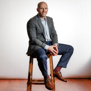 professional man wearing navy and red shadow stripe dress socks with business casual attire sitting on stool