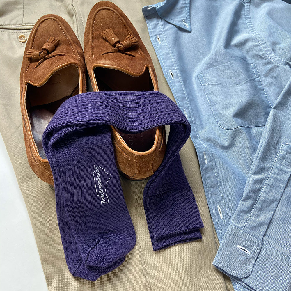 pair of purple dress socks atop suede tassel loafers and folded business casual clothing