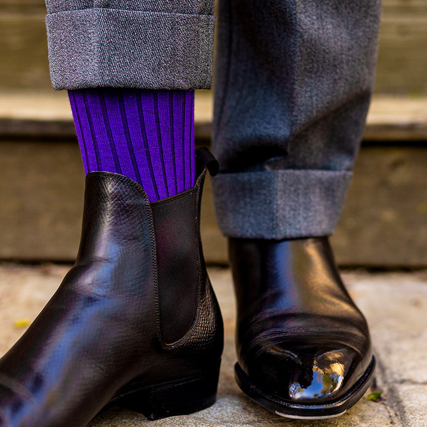 man lifting pant leg to show purple dress socks paired with his dark brown chelsea boots
