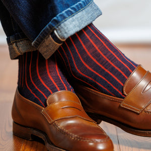 man crossing ankles wearing navy and red shadow stripe dress socks with jeans and penny loafers