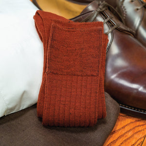 pair of Burnt Orange Merino Wool Mid Calf Dress Socks laying on top of nice clothing