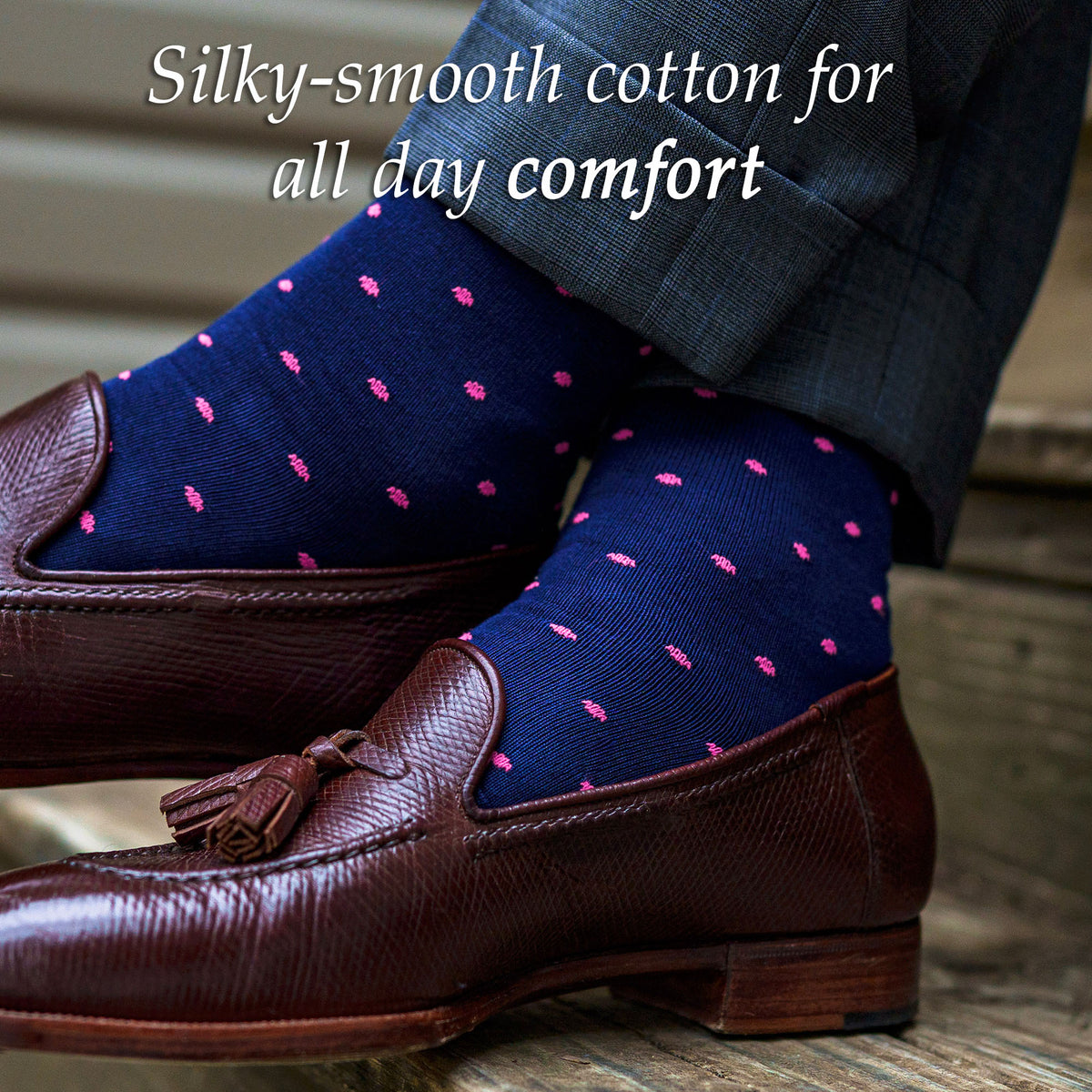 man wearing navy cotton dress socks decorated with bright pink polka dots crossing ankles