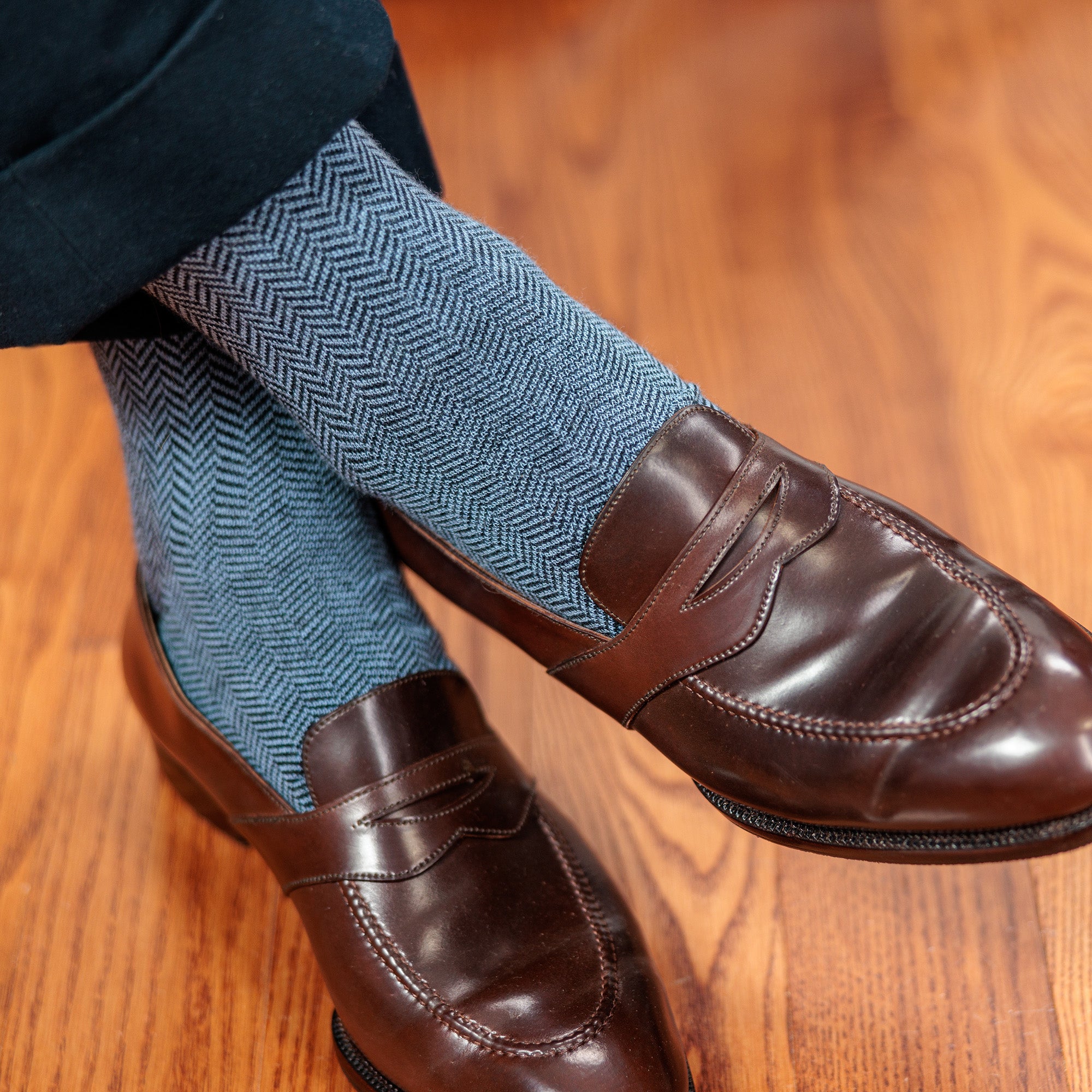 light blue and black herringbone dress socks paired with dark penny loafers and charcoal slacks