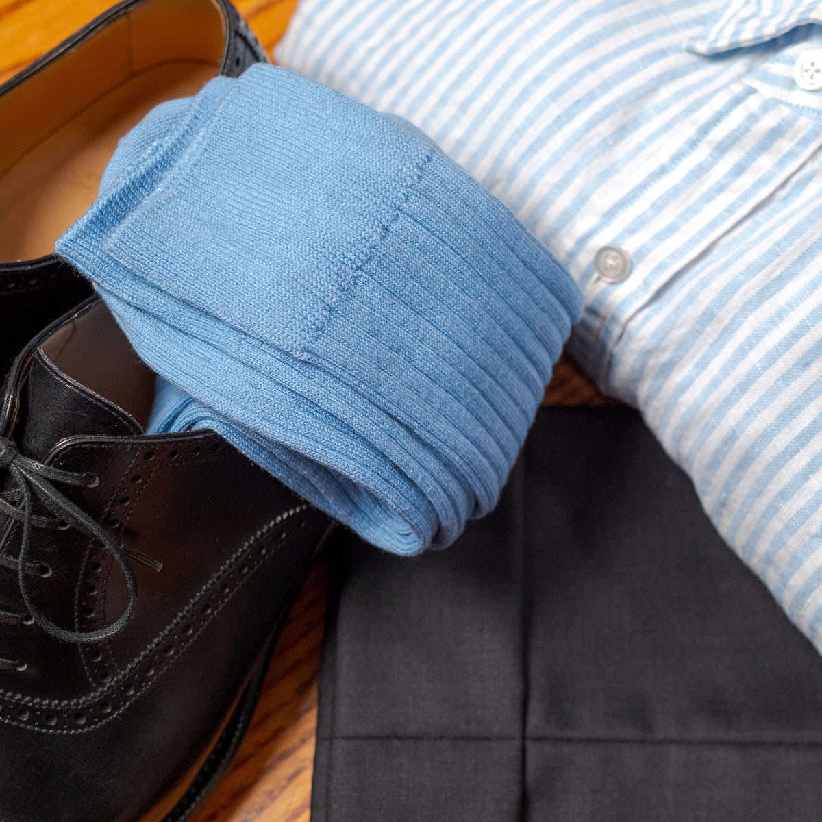 light blue ribbed dress socks situated on hardwood floor with grey slacks black oxfords and a blue and white striped button down