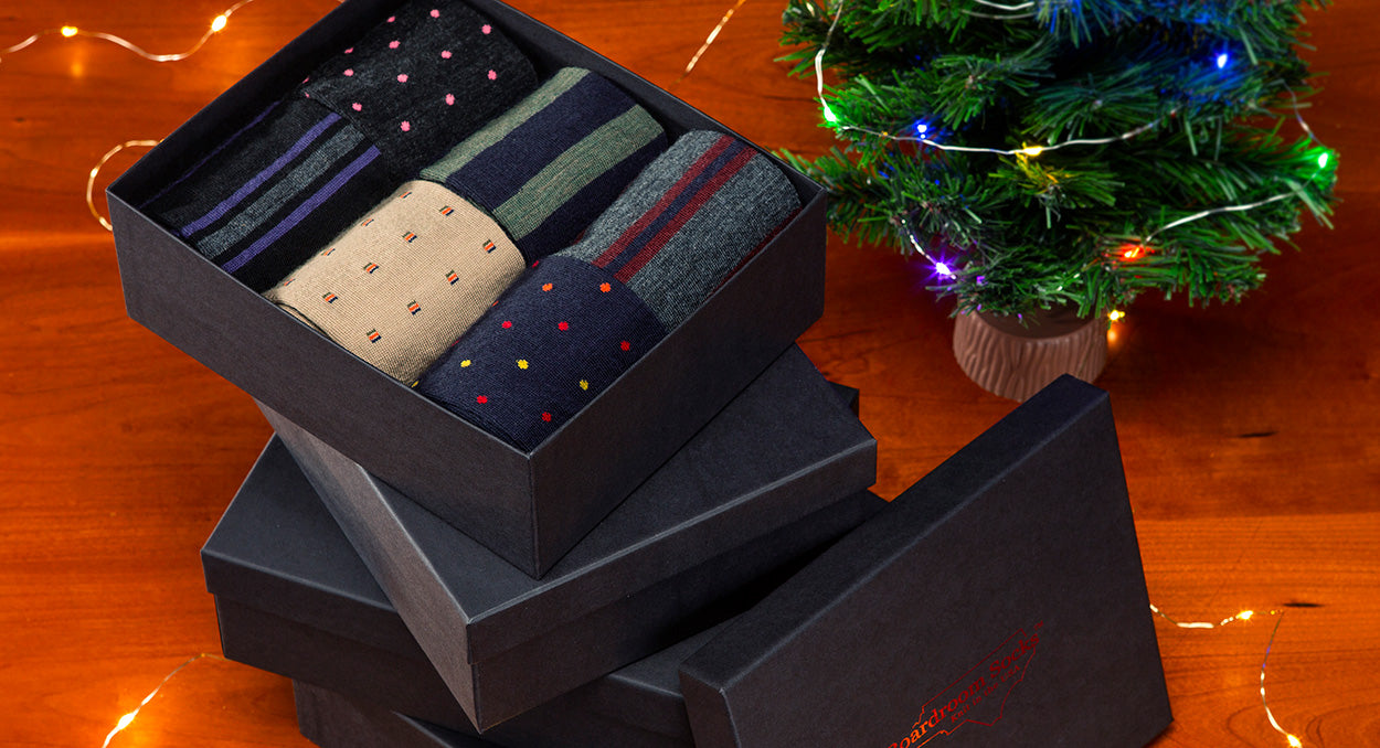 stack of gift boxes filled with colorful merino wool dress socks surrounded by holiday decor