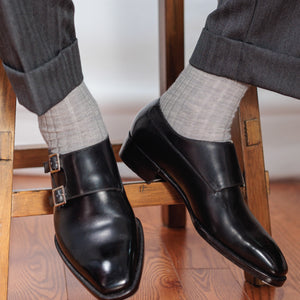 image of a man who is sitting on a stool wearing nice black dress shoes, grey slacks, and light grey over the calf wool dress socks