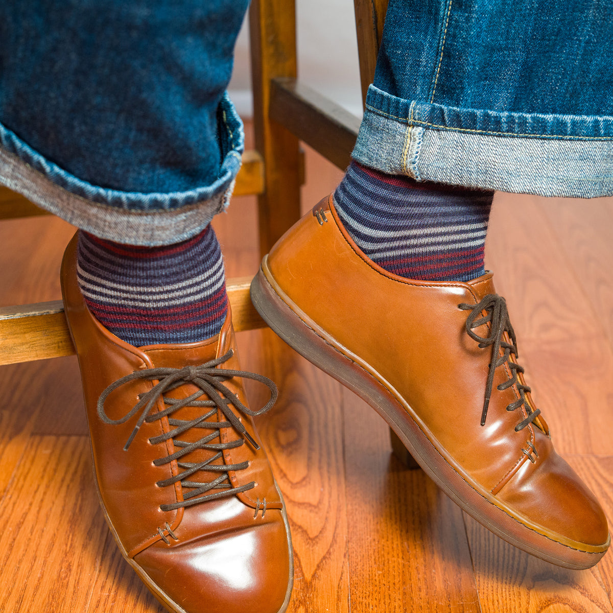 man wearing colorful striped dress socks with jeans and brown leather shoes while seated on a stool