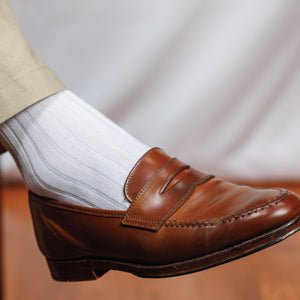 man's right foot wearing brown loafers and white ribbed knit cotton over the calf socks