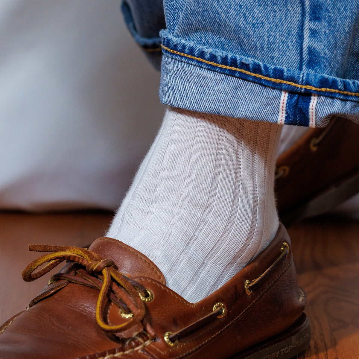 left foot of a person wearing white merino wool dress socks and boat shoes