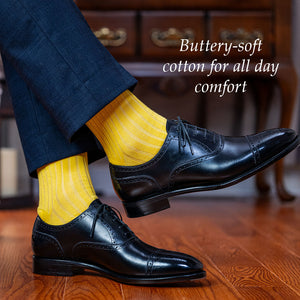 man crossing legs wearing yellow cotton dress socks with black oxfords and a navy suit