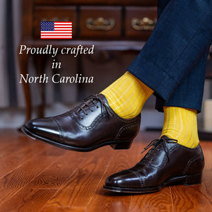 man crossing legs wearing yellow cotton dress socks with a navy suit and dark brown oxfords