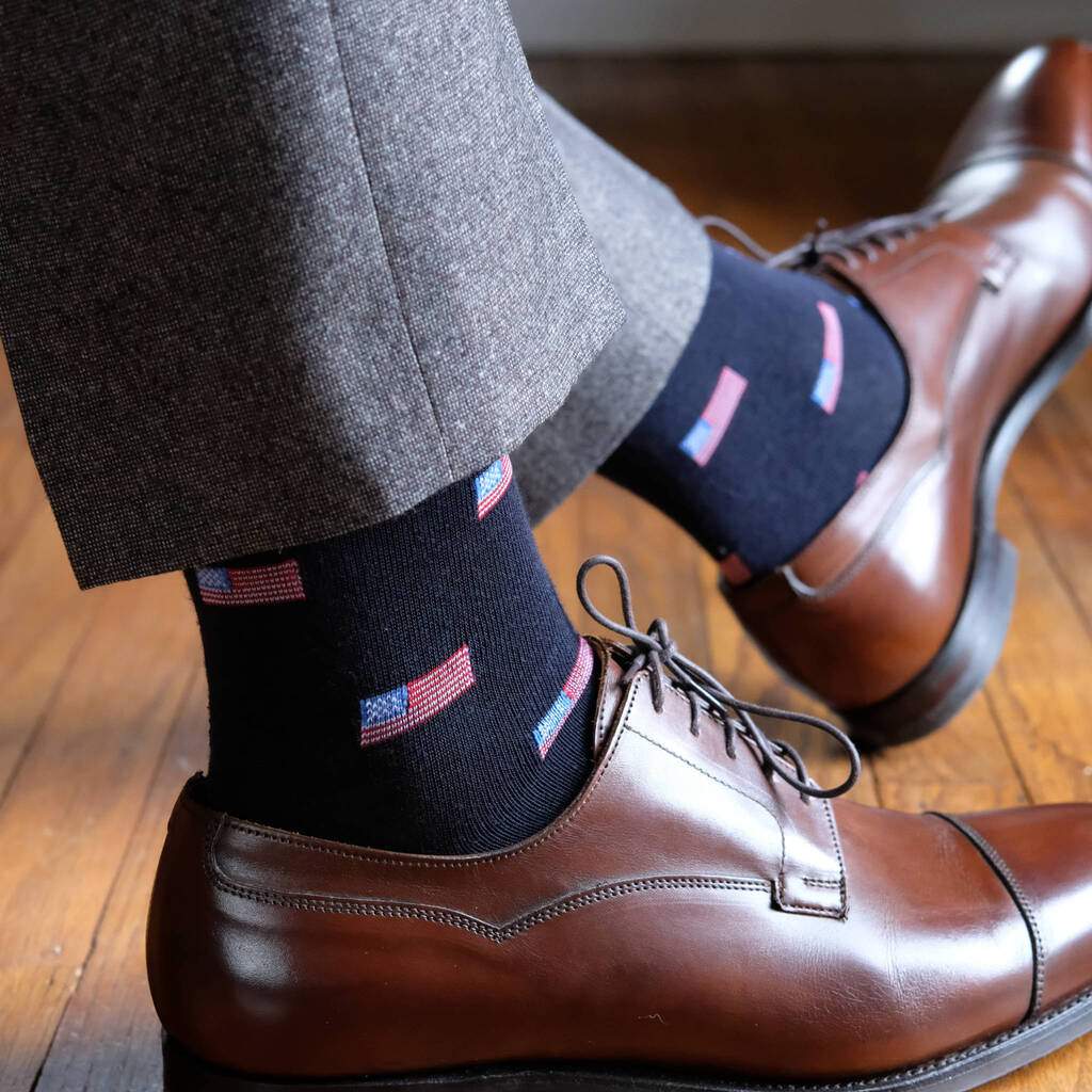 Man Wearing Grey Dress Pants and Dark Brown Dress Shoes with Navy Blue Dress Socks Accented with Small American Flags