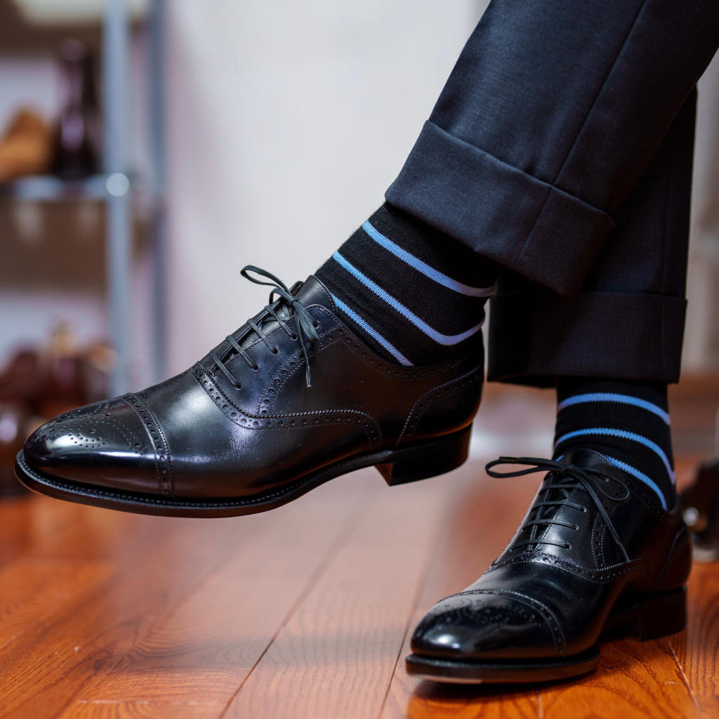 man crossing legs wearing black and blue striped dress socks with black oxfords