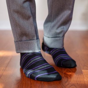 man wearing black dress socks with purple and grey stripes walking on hardwood floors