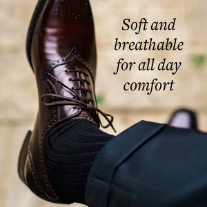man crossing legs wearing black cotton dress socks with dark grey trousers and burgundy brogue dress shoes