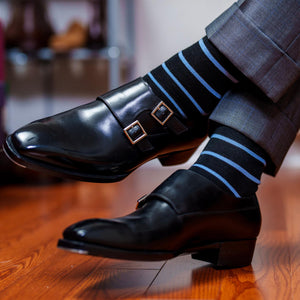 man crossing ankles wearing black and blue striped dress socks with grey trousers and black double monkstrap shoes