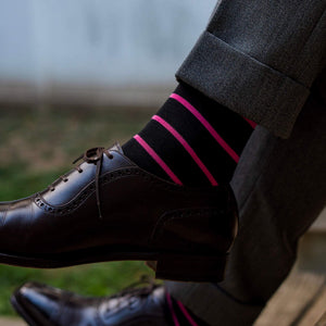 man crossing legs wearing black dress socks with bright pink stripes