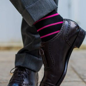 man wearing black dress socks with bright pink stripes crossing ankles