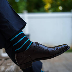 man crossing legs wearing black dress socks with bright blue socks and navy trousers